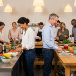 Diverse group happily cooking in a modern, well-lit kitchen studio, collaborating during a team building workshop with fresh ingredients.
