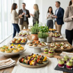 Elegant organic cocktail dînatoire spread with mini quiches, vegetable skewers, and verrines on a wooden table. Professionals mingle in background.
