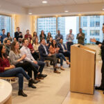 A director delivers an inspiring year-end speech to a diverse, applauding team in a festive, modern conference room.