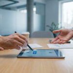 Deux personnes en réunion signent un document sur une tablette avec un stylet, l'écran affiche "APPROVE" et des cadenas.